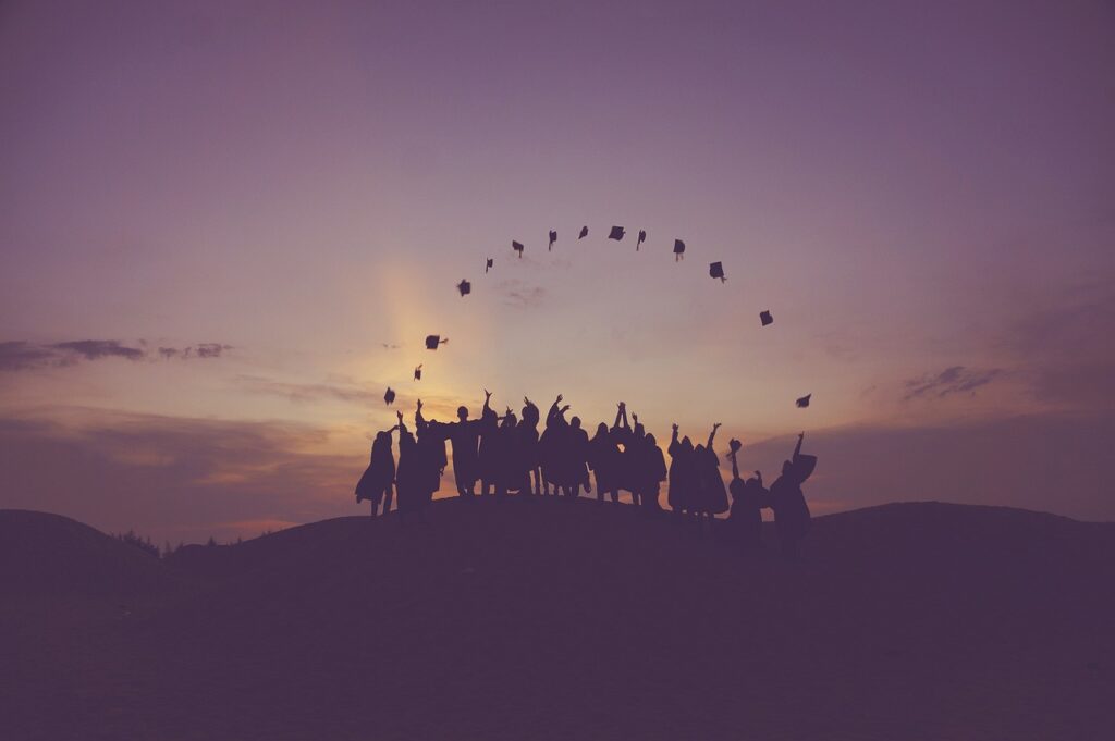 Gün batımında havaya şapka fırlatarak Abitur'larını kutlayan siluetli bir grup insan.