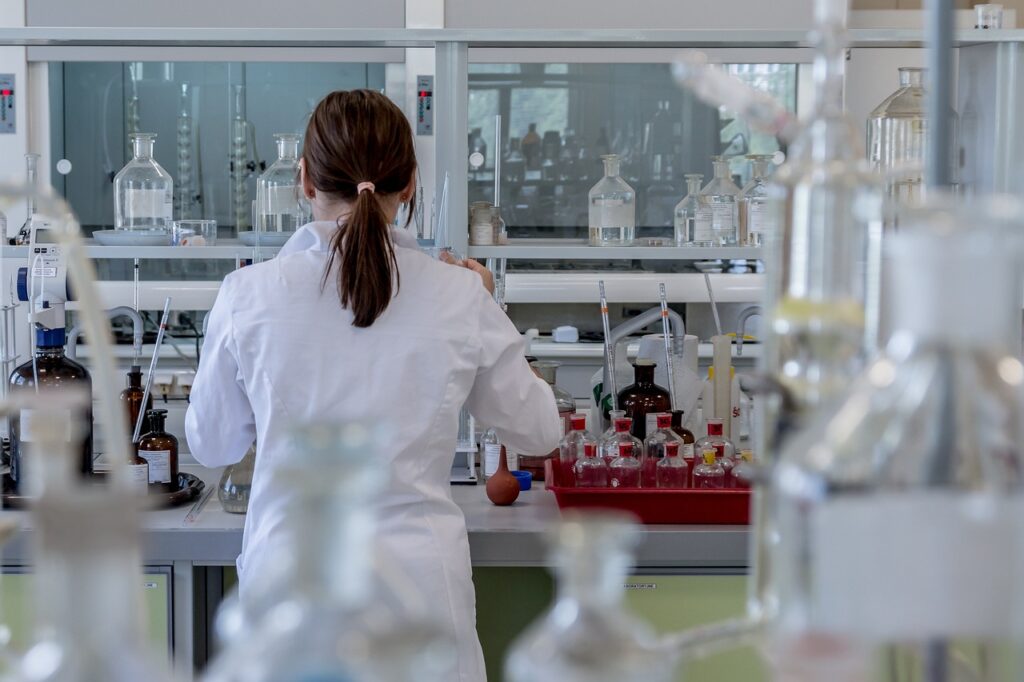 Bir laboratuvarda çeşitli cam eşyalar arasında çalışan, önemli başarılarından dolayı onay alan, beyaz laboratuvar önlüğü giyen bir bilim adamı.