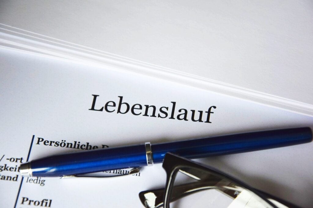 Almanca "özgeçmiş" anlamına gelen "Lebenslauf" başlığını taşıyan bir belgenin üzerinde duran bir kalem ve gözlük.
