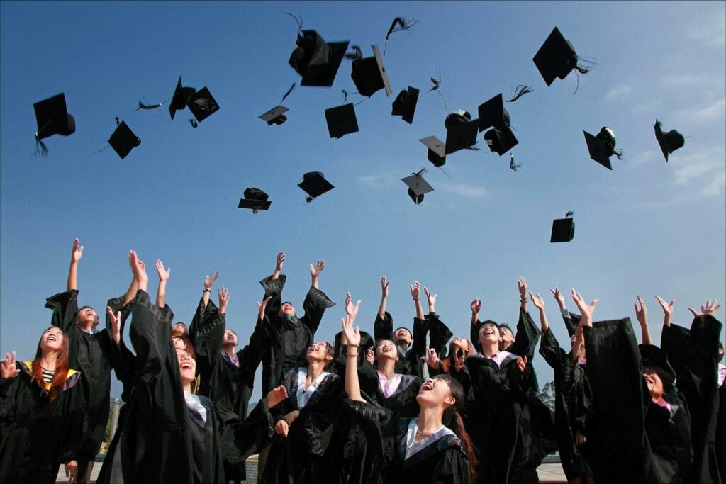 Mezuniyetlerini şapkalarını havaya fırlatarak kutlayan bir grup mezun.