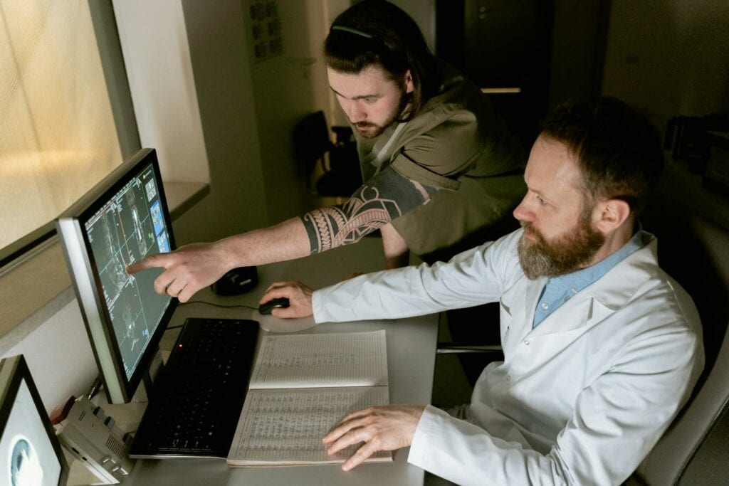 Laboratuvar önlüğü giymiş iki adam, Almanya'da Tıp Okumak Başvuru Süreci için Detaylı Rehber'i anlamak üzere bilgisayar ekranına bakıyor.